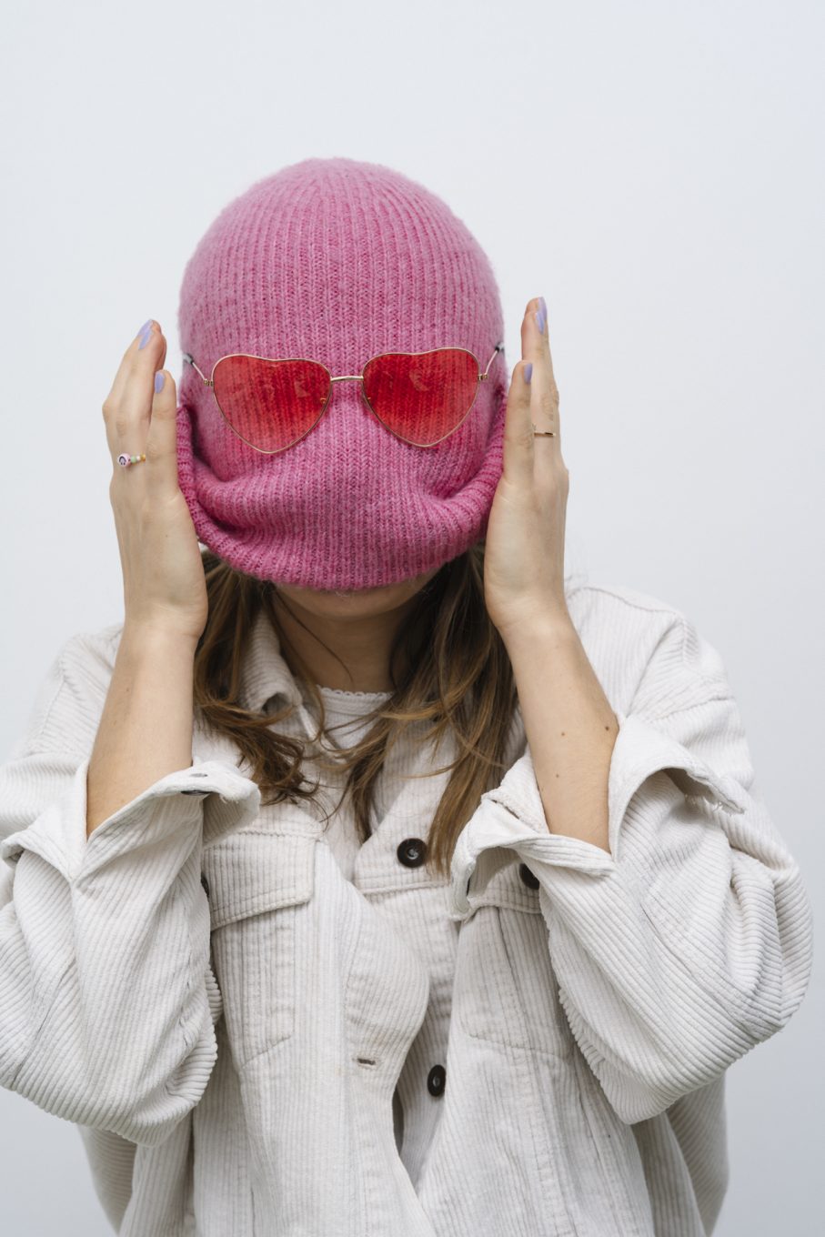woman with pink knitted cap pulled up over face and pink heart sunglasses