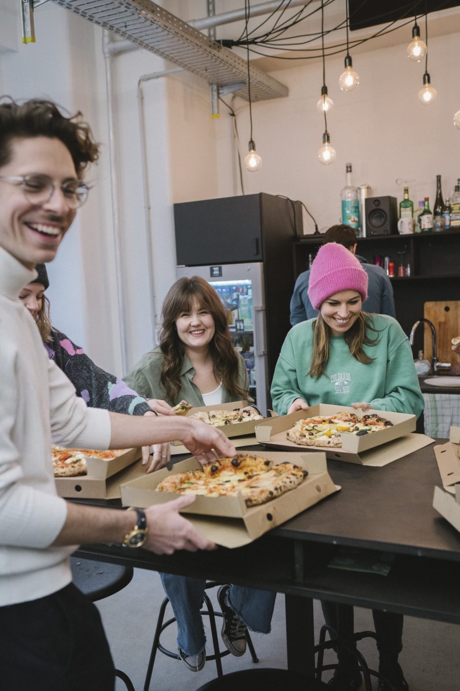 Drei junge Menschen an einer Kücheninsel essen Pizza